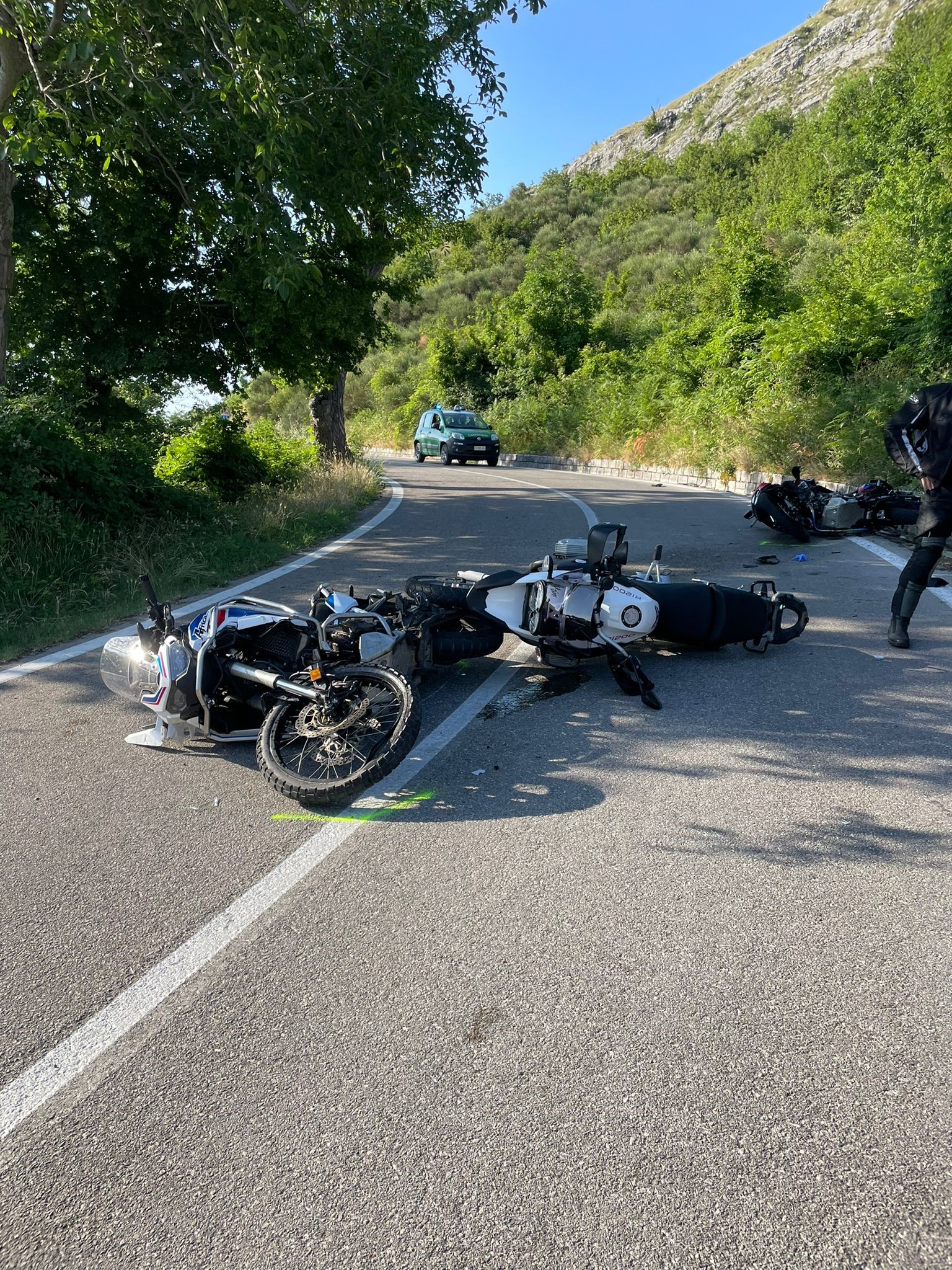 Due motocicli a terra su strada extraurbana con marcature a terra e forze dell'ordine impegnate nei rilievi