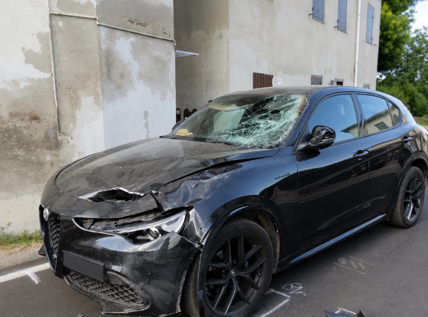 Autovettura con parabrezza sfondato e cofano deformato, con tracciamenti a gesso sull'asfalto eseguiti durante i rilievi